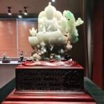 This serene Guanyin sits gracefully on a lotus throne, holding a blossom. An emerald dragon and luminous pearl flank her side, while a carved back halo frames her form. The wooden base, engraved with intricate Buddhist sutras, perfectly enhances the sculpture’s divine and tranquil aura.