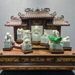 The Nine‑Dragon Imperial Seal is a large jadeite antique‑style carving. The set comprises multiple seal stamps carved with dragons, auspicious beasts and other mythical creatures, linked by intricately carved movable chains. The jade is warm and lustrous, with vivid green in select areas. It rests on an exquisitely crafted wooden pedestal and archway. With elaborate, sophisticated workmanship that recreates the majesty of ancient imperial seals, the piece showcases the supreme artistry of traditional jade carving and the cultural significance of royal authority.